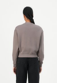 Gray sweatshirt with ribbed cuffs and hem. Soft fabric, relaxed fit, cropped design. Worn with dark denim pants in a neutral backdrop.