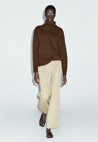 Brown knitted turtleneck sweater, oversized fit, paired with beige wide-leg trousers and brown flat sandals. Minimalistic design with soft textures.
