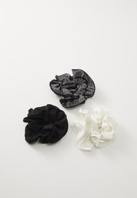 Drie haarscrunchies: één van zwarte stof, één van witte stof en één zwart met een textuurpatroon in zilver en randen. Zacht, gelijkmatig ontwerp.