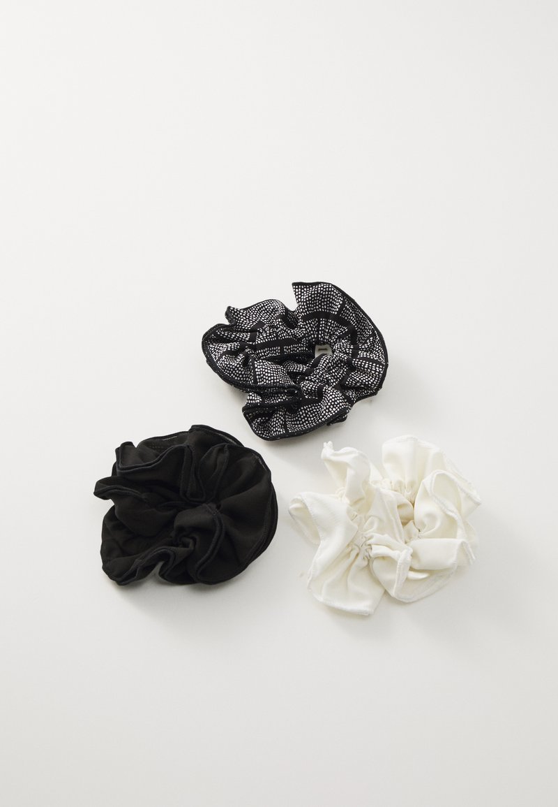 Drie haarscrunchies: één van zwarte stof, één van witte stof en één zwart met een textuurpatroon in zilver en randen. Zacht, gelijkmatig ontwerp.