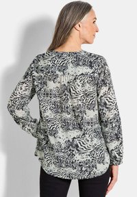 Langärmlige Bluse aus einem gemusterten schwarzen und hellcremefarbenen Stoff, mit abstrakten Designs und einem lässigen Schnitt mit abgerundetem Saum.