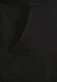Sort sweatshirt med kangaroo-lomme, ribbet kant og glat stofftekstur. Synlige stingdetaljer langs lommens kanter.