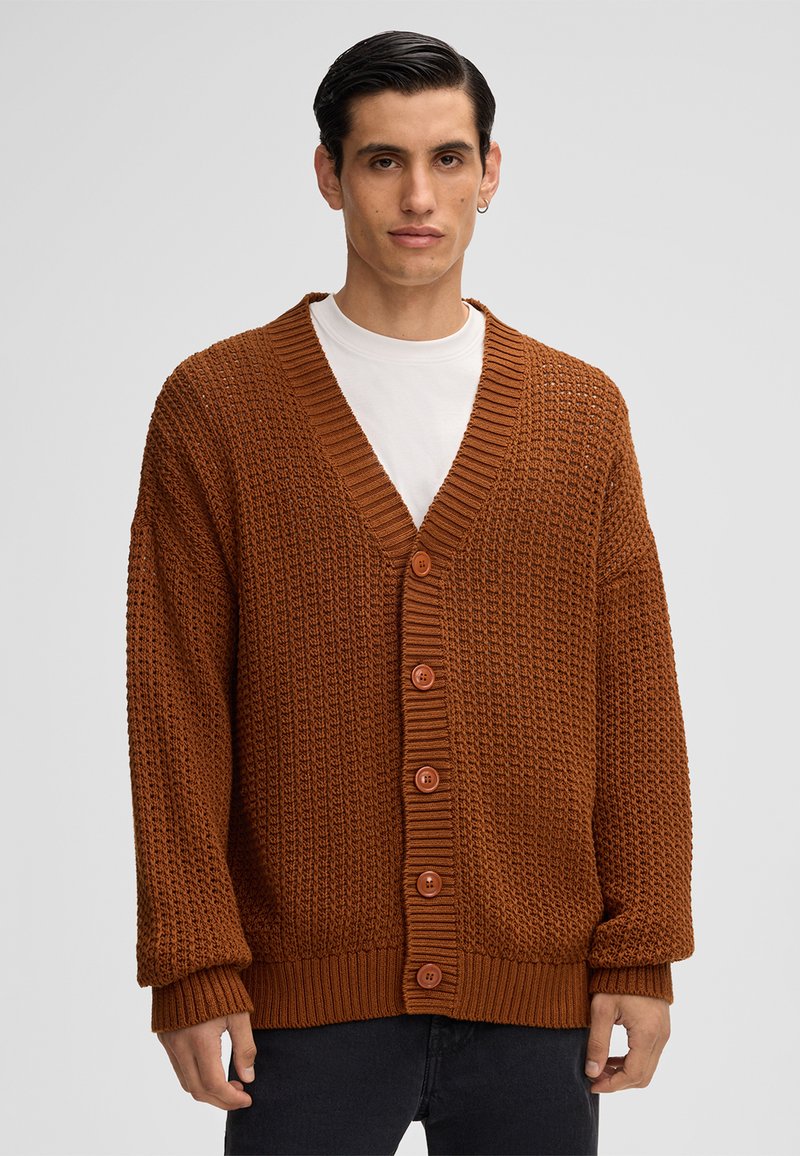 Cardigan lavorato a maglia marrone con scollo a V, polsini a coste e cinque grandi bottoni. Presenta motivi testurizzati su tutta la stoffa.