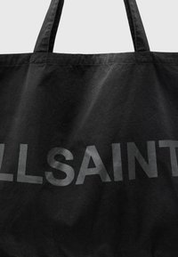Zwarte schoudertas van canvas, met grote, matte zwarte "ALLSAINTS" letters aan de voorkant. Inclusief stevige schouderbanden.