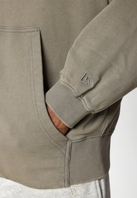 Oliven grøn sweatshirt med ribstrikkede manchetter og bund, kengurulomme og broderet logo på ærmet. Blødt stof.