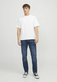 Camiseta blanca de algodón con manga corta combinada con jeans de denim azul. Las zapatillas presentan colores negro y blanco, realzando el estilo casual.
