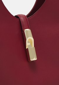 Sac à main en cuir rouge avec une texture lisse, présentant un détail de fermeture à verrou métallique doré et une anse courbée.