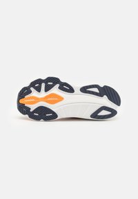Skoens yttersåle har en hvit base med et strukturert mørkeblått og oransje gummimønster for grep og holdbarhet. "Saucony" er preget.