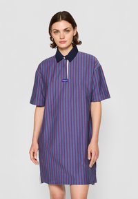 Vestido riscado com linhas verticais em vermelho, azul e branco, colarinho azul-marinho, mangas curtas e uma etiqueta de logo na parte frontal.