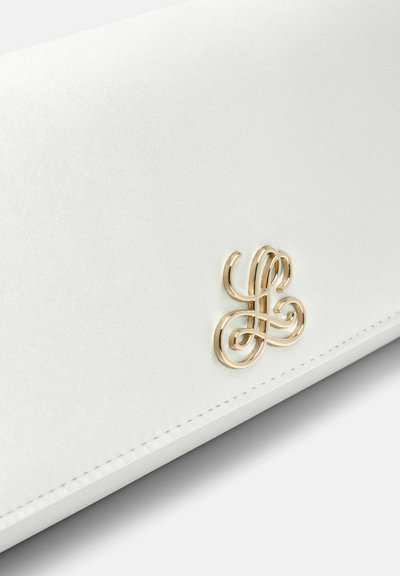 Surface en cuir blanc avec une fine couture et un petit logo ornemental doré présentant des lettres entrelacées en style cursif.