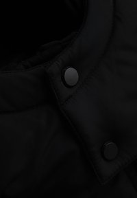 Collo del giubbotto puffo nero realizzato in tessuto liscio e opaco, con bottoni a pressione neri circolari e cuciture rinforzate per una maggiore resistenza.