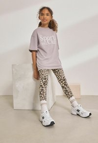 Szürke, oversized póló "Sports Club 1982" felirattal, párosítva leopárdmintás leggings-szel és fehér, fekete részletekkel rendelkező sneakerrel.
