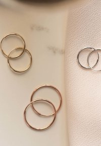 Drie paar hoepeloorringen in goud, roségoud en zilver. Het oppervlak is glanzend met een circulair ontwerp. Een zachte stof is op de achtergrond.