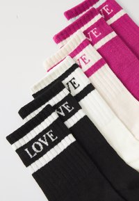 Χρωματιστές κάλτσες σε μαύρο, λευκό, ροζ και κρέμα με έντονο κείμενο "ΑΓΑΠΗ" και ριγέ μοτίβα στην κορυφή. Φτιαγμένες από μαλακό, ριγωτό υλικό.