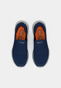 Παπούτσια Skechers slip-on σε ναυτικό μπλε με γκρι σόλα. Το εσωτερικό διαθέτει πορτοκαλί επενδυμένο πάτο. Ελαφρύ, αεριζόμενο σχέδιο.