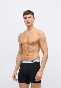 Fekete boxernadrág világoskék Nike logóval díszített derékpánttal, puha, ruganyos anyagból készült. A test tónusos és nem visel inget.