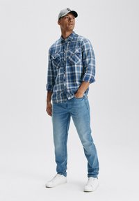 Niebieska koszula w kratę w biel i niebieskości, z dwoma kieszeniami na piersi, połączona z jasnoniebieskimi dżinsami i białymi trampkami. Z szarym kapeluszem.