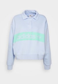 Ljust blå, kort sweatshirt med krage, med ett grönt band och vit "adidas"-logotyp. Mjuk, bomullsmaterial med ribbade ärmslut.