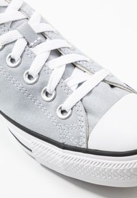 Baskets en toile grises avec lacets blancs, œillets en métal, embout en caoutchouc et semelle en caoutchouc noire avec un design texturé.