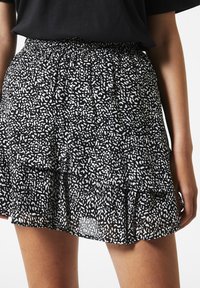 Jupe à plusieurs niveaux en noir et blanc, en tissu léger, avec un motif éparpillé et une taille élastique. L'ourlet est légèrement effiloché.