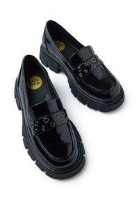 Mocasines de charol negro con suelas de goma gruesas, que presentan ojales decorativos de plata en una cinta ancha a través del empeine.
