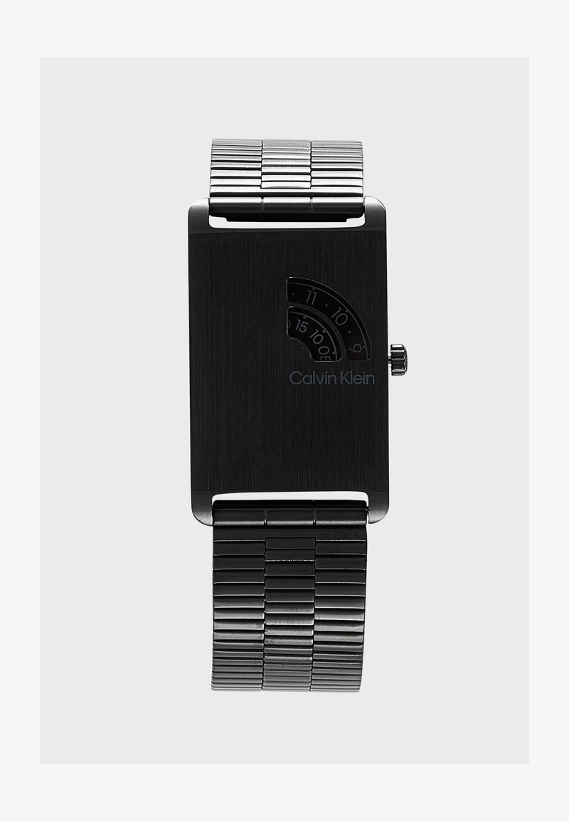 Montre-bracelet rectangulaire noire Calvin Klein avec bracelet en métal et petit cadran en demi-cercle affichant les heures et les minutes.
