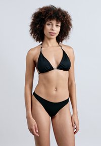 Μαύρο σετ μπικίνι με τριγωνικό τοπ και ρυθμιζόμενους ιμάντες, καθώς και αντίστοιχο ριμπάτ κάτω μέρος. Το ύφασμα είναι λείο και ελαστικό.