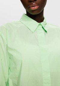 Camicetta verde chiaro con colletto realizzata in tessuto liscio, con chiusura a bottoni e un design dalla vestibilità rilassata.