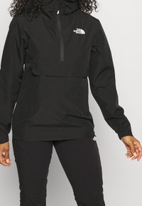 Czarna wodoodporna bluza przeciwwiatrowa z suwakem z przodu, regulowanym kapturem i logo na piersi. Posiada elastyczne mankiety i luźny krój.