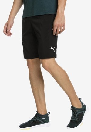 Czarne sportowe spodenki o gładkiej fakturze, wyposażone w boczne kieszenie oraz biały logo marki Puma na dolnej części lewej nogawki.