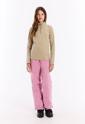 Beige fleece pullover met een rits tot de helft, gecombineerd met roze waterdichte broek. Zwarte winterlaarzen maken de outfit compleet.