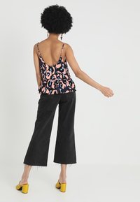 Top peplum sans manches en imprimé animal rose et noir, avec un dos décolleté, associé à un jean large noir et des mules à talons blocs jaunes.