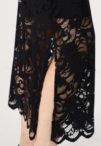 Mustmustest mustriks lilledega, millel on reie kõrguseni lõhik ja laineline ääreline. Kerge, õhuke tekstuur, elegantne disain on hästi nähtav.