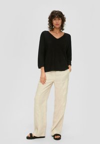 Schwarzer V-Ausschnitt-Pullover mit langen Ärmeln, kombiniert mit lockeren beigen Leinenhosen und schwarzen Plateau-Sandalen. Glatte Textur, entspannter Schnitt.