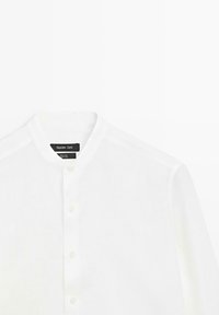 Chemise blanche en lin à manches longues avec col mao, boutonnée sur le devant, avec étiquette de la marque Massimo Dutti visible à l'intérieur du col.
