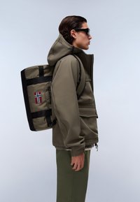 Veste imperméable vert olive avec capuche, accents noirs et sac à dos intégré, ornée d'un patch du drapeau norvégien et d'un design épuré.