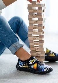 Buntes schwarzes Slipper-Schuhe mit dem Text "SPEED", versehen mit einem Rennwagen-Graphic und kreisförmigen Mustern. Passt gut zu Jeans und gestapelten Jenga-Blöcken.