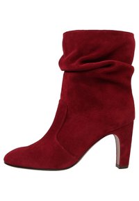 Botín de ante rojo hasta el tobillo con un diseño arrugado, punta afilada y un alto tacón de aguja. Presenta una textura suave y un estilo sin costuras.