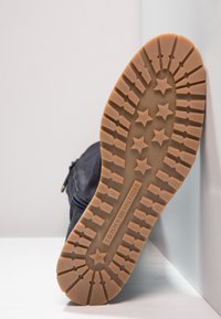 Suela de sneaker de goma marrón con un patrón de estrellas, que cuenta con estrías para mayor tracción. Detalle de cremallera en el lado, cuerpo de tela oscura visible.