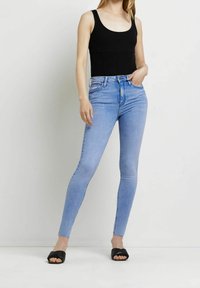 Top sin mangas negro ajustado, jeans de talle alto azul claro, diseño ajustado, textura de denim suave, combinado con sandalias deslizantes negras.