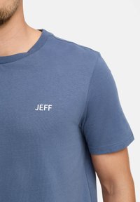Maglietta in cotone blu con maniche corte, colletto rotondo e un piccolo logo bianco "JEFF" sulla zona sinistra del petto. Tessuto morbido.