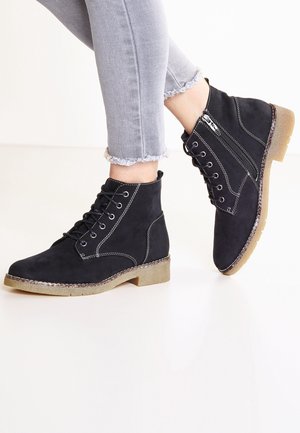 Černé kotníkové boty z semiše s texturovaným povrchem, bílým stehem a zaoblenou špičkou. Mají boční zip a průhlednou, texturovanou gumovou podrážku.