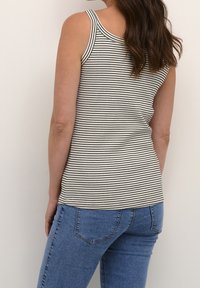 Gestreiftes Top in Creme und Schwarz, gerippte Textur, mit breiten Spaghettiträgern. Kombiniert mit blauen Jeans aus Denim. Keine sichtbaren Muster auf den Jeans.