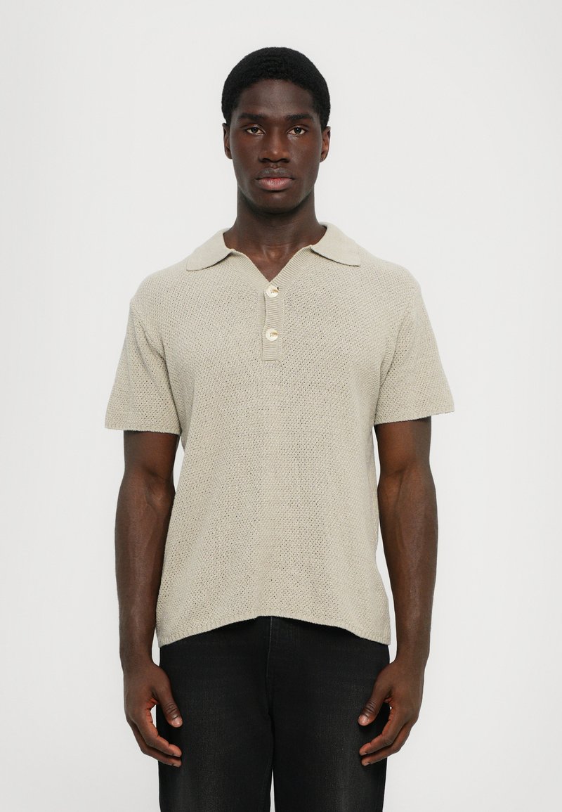 Ανοιχτό μπεζ πλεκτό polo μπλουζάκι με γιακά, κοντά  μανίκια και τρία κουμπιά στο λαιμό. Με υφή και χαλαρή εφαρμογή.