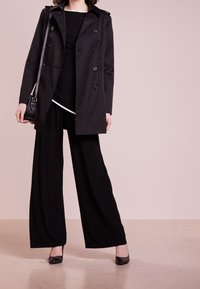 Svart dubbelknäppt kappa, lång svart topp, vida svarta byxor och svarta klackar. Texturerad tyg, slät yta och minimalistisk design.