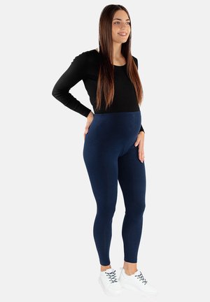 Legginsy ciążowe w kolorze granatowym, elastyczny materiał, wysoki stan, zestawione z czarną długą bluzką i białymi trampkami. Gładka struktura.