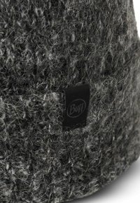 Dark gray knitted beanie with textured yarn, featuring a small black leather tag with "Buff" logo on the side. Soft and fuzzy appearance.