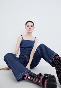 Džínový outfit pozostávajúci z priliehavého tmavomodrého tielka s tenkými šnúrkami a voľných tmavomodrých džínsoch. Znateľné lesklé čierne a ružové čižmy na zips.