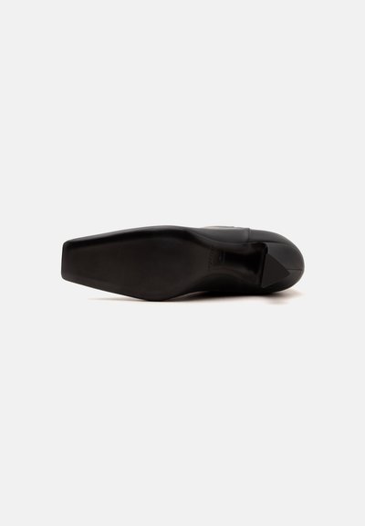 Chaussure de ville en cuir noir avec un large bout carré et une semelle lisse, vue de dessous sur fond blanc.