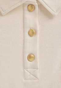 Polo beige con texture a coste, dotata di tre bottoni dorati con motivi in rilievo e colletto cucito.